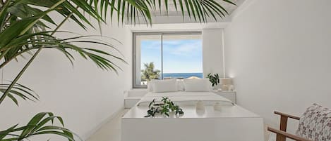 A modern bedroom with a large window, a bed, and a view of the sea.