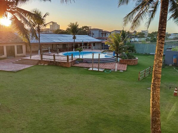 A backyard with a swimming pool, a covered patio, and a grassy lawn. - pousada vila real (São Mateus)