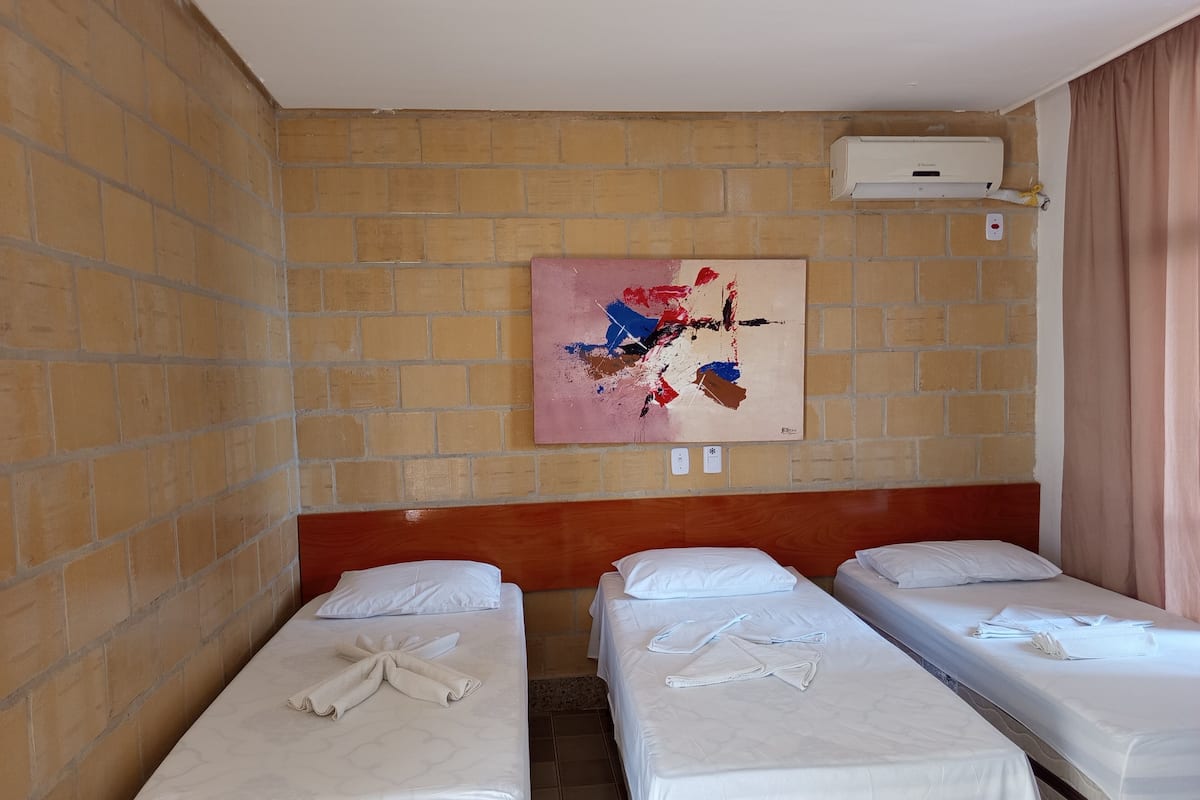 A hotel room with two single beds, a brick wall, a painting, and an air conditioning unit.