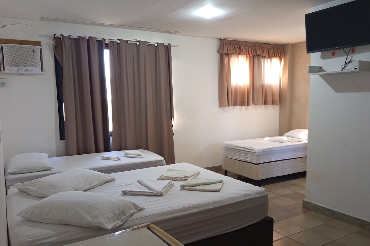 Habitación de hotel con dos camas, un televisor de pantalla plana montado en la pared y una ventana con cortinas.