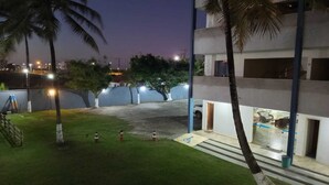 Vista nocturna de un edificio con un patio arbolado, palmeras y una zona de estacionamiento.
