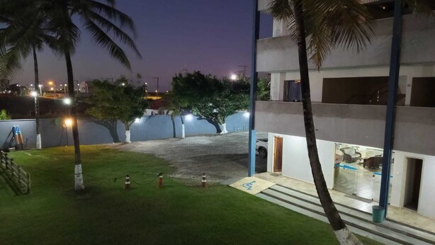 A nighttime view of a building with a grassy courtyard, palm trees, and a parking area.