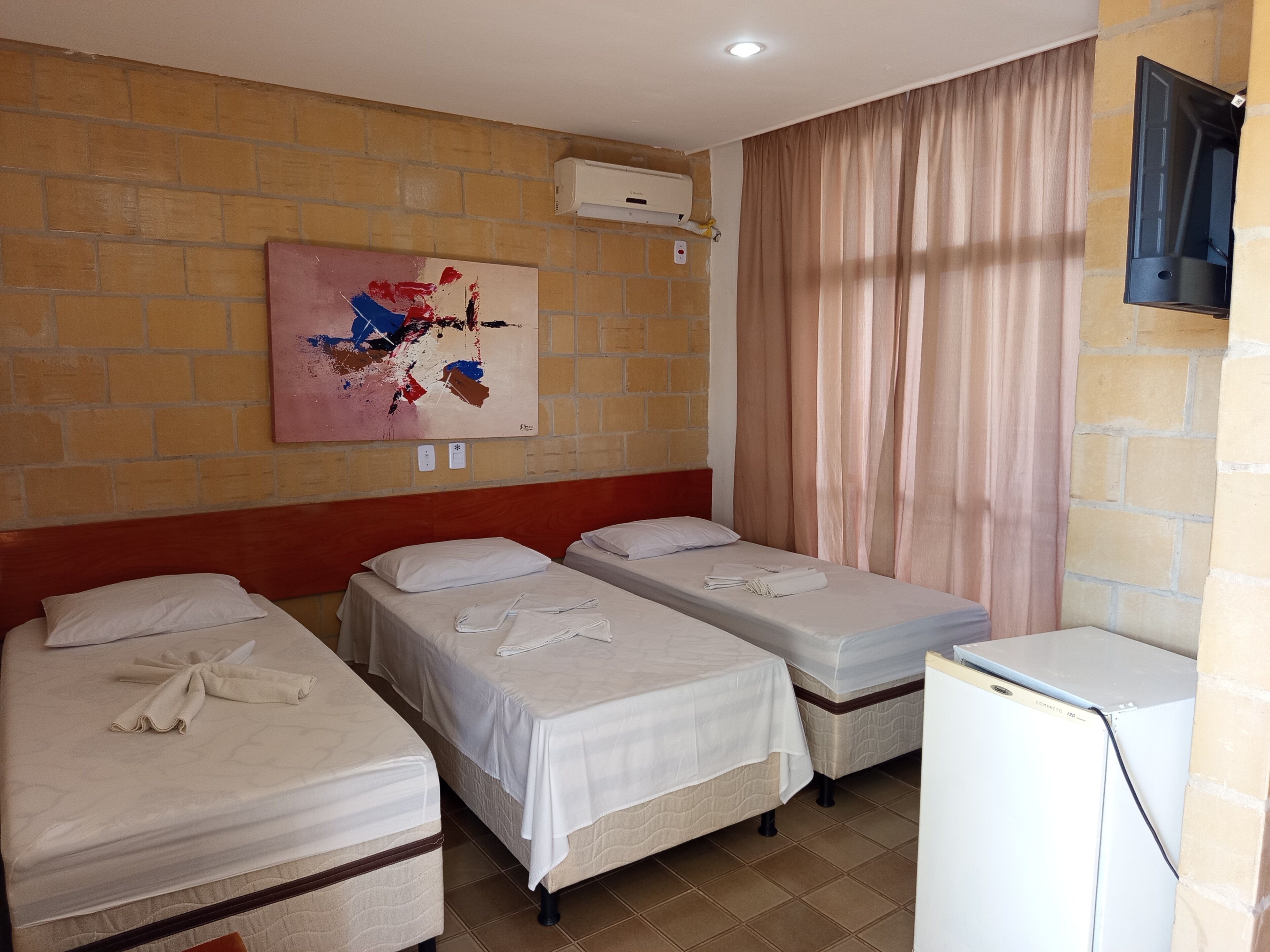 Habitación de hotel con tres camas, un televisor de pantalla plana, un aire acondicionado y un cuadro en la pared.