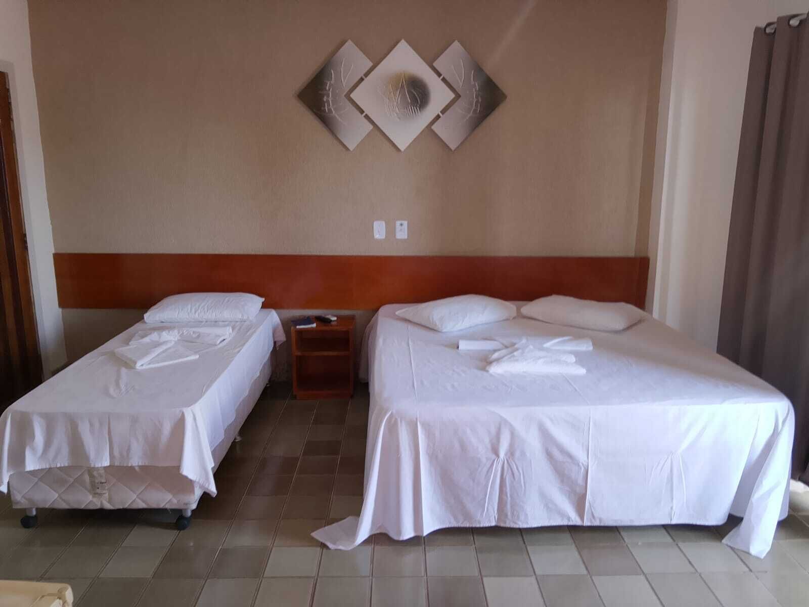 A hotel room with two beds, a wooden headboard, a wall-mounted light switch, and a decorative wall piece.