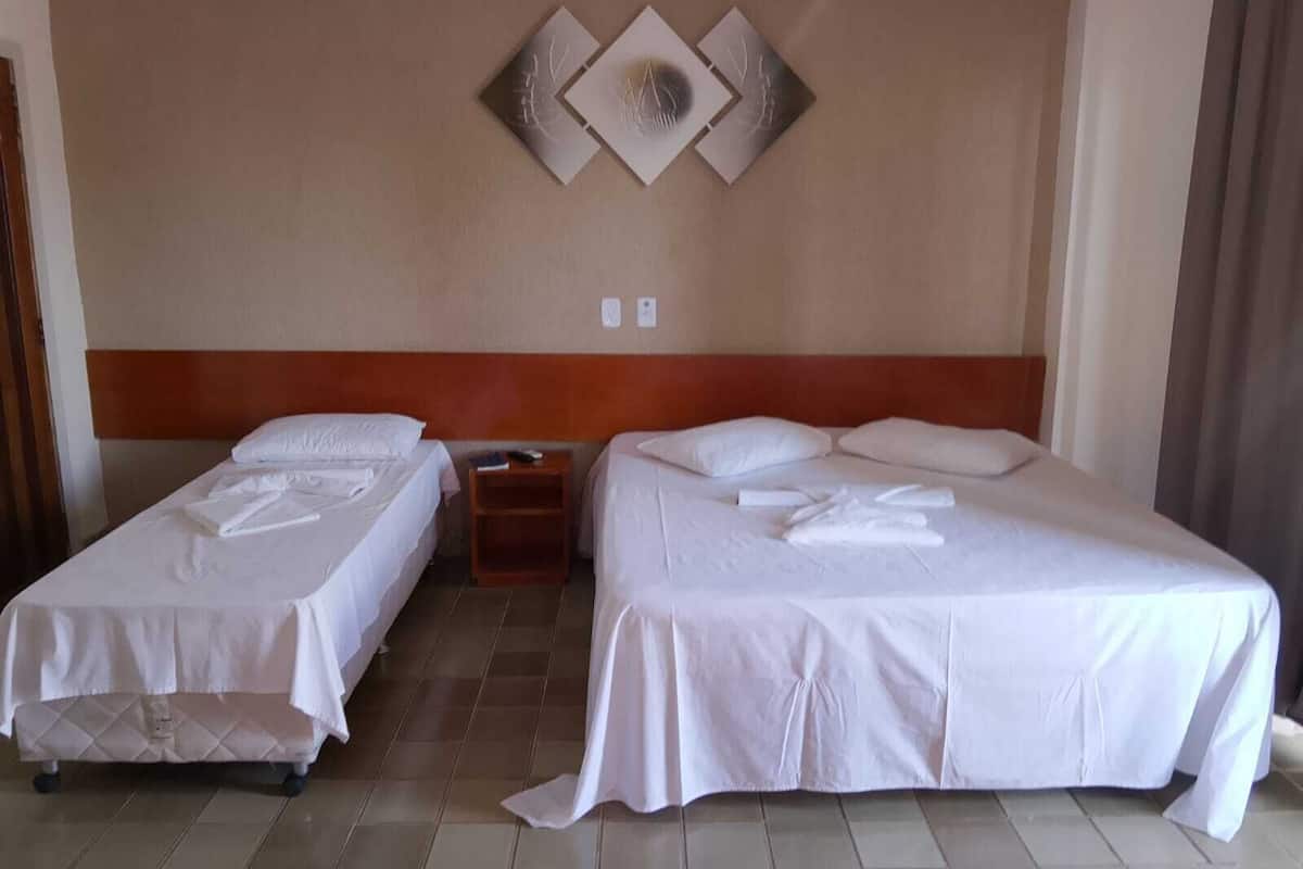 A hotel room with two beds, a wooden headboard, a wall-mounted light switch, and a decorative wall piece.