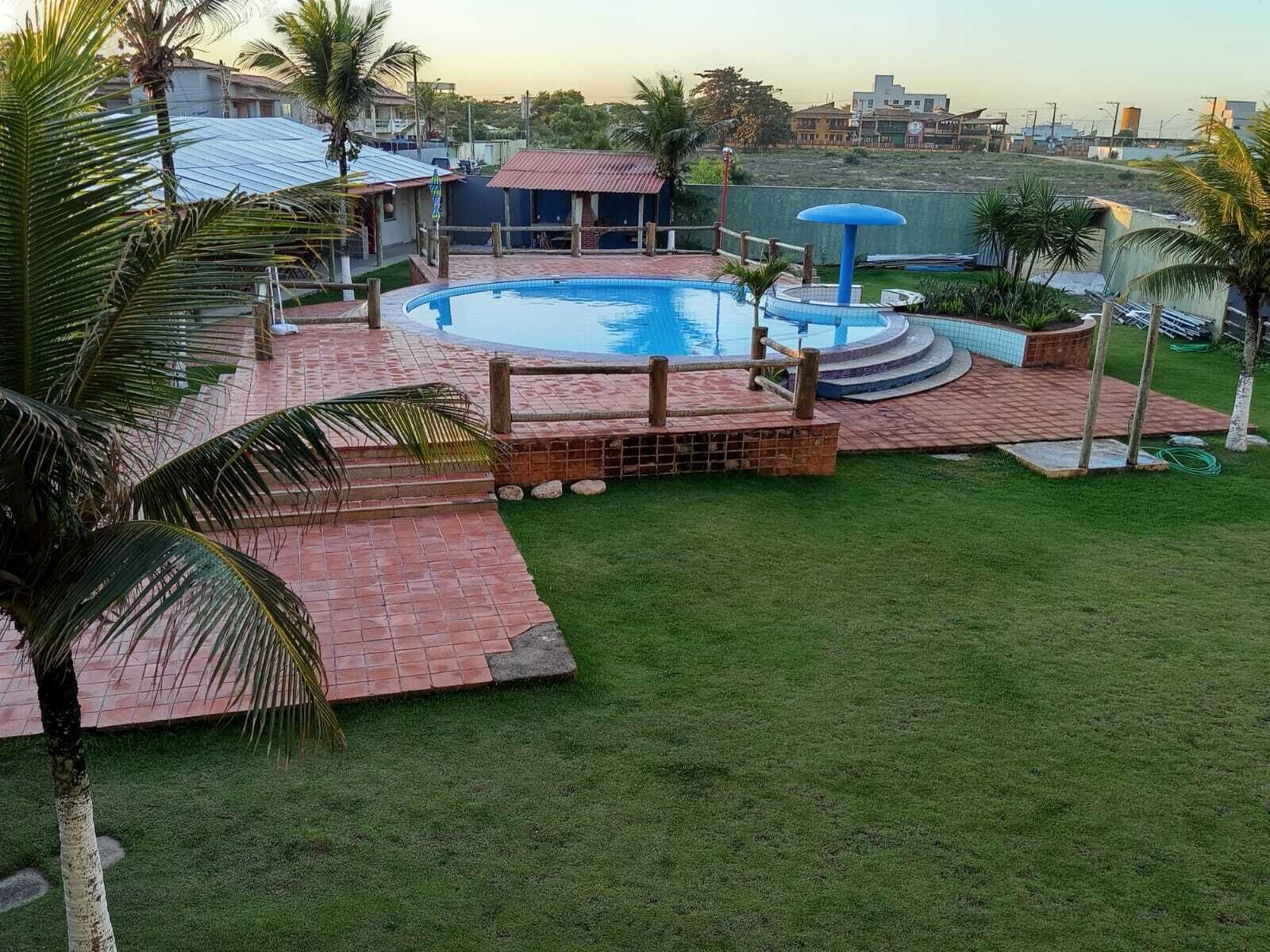 Una piscina con cubierta de madera, rodeada de césped y palmeras.