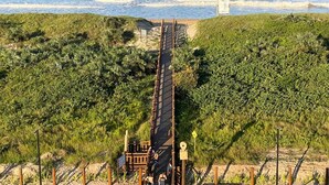 A coastal walkway leading to a beach with a small structure nearby.