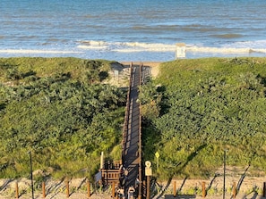 A coastal walkway leading to a beach with a small structure nearby.