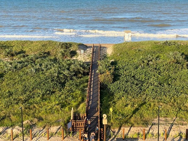 A coastal walkway leading to a beach with a small structure nearby. - pousada vila real (São Mateus)