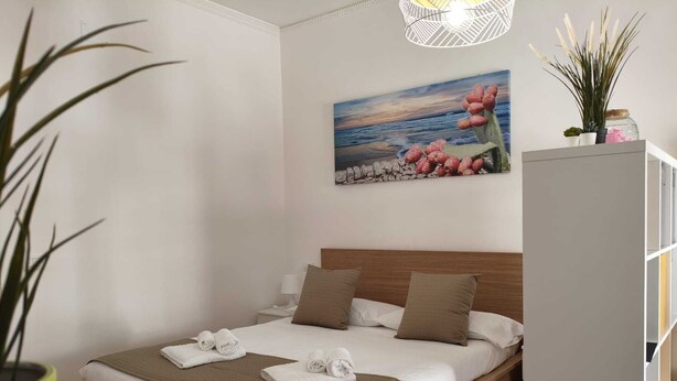 Ein Schlafzimmer mit Bett, Kissen, Nachttisch, einem Gemälde, einer Pflanze und einem Schrank.