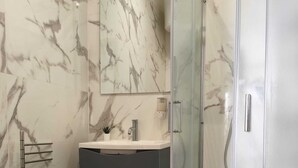 Ein Badezimmer mit Marmorwand, einer Duschkabine aus Glas, einer Toilette und einem Waschbecken mit Spiegel darüber.