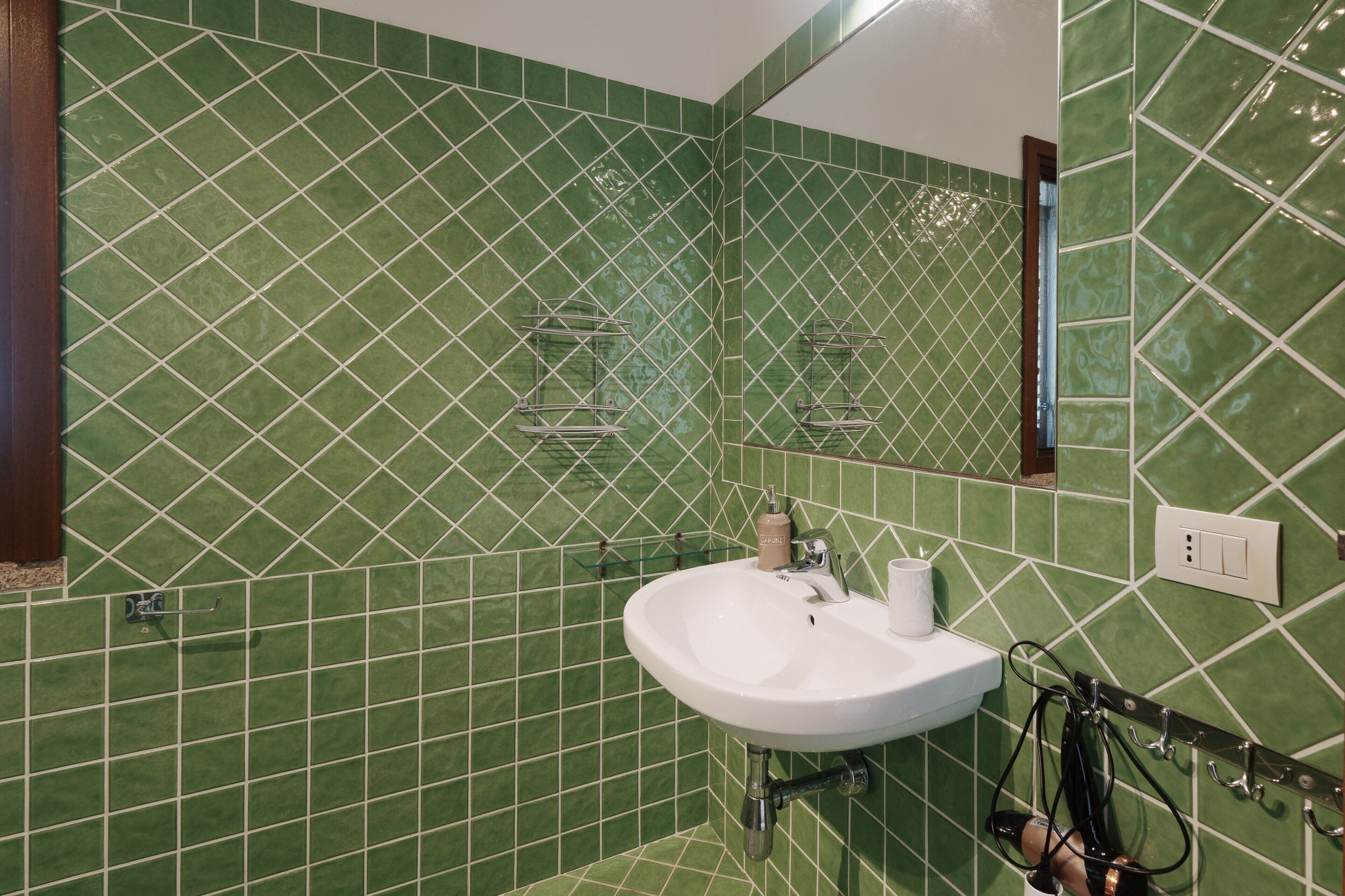 Un bany amb parets de rajola verd, un lavabo blanc i un mirall.