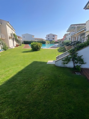 Zona residencial con piscina, césped bien cuidado y edificios de varios pisos.