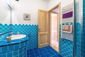 A bathroom with a blue-tiled floor, a white sink, and a wooden door. - Holiday Home 'Il Gabbiano Perle Gallura' with Air Conditioning (Palau)