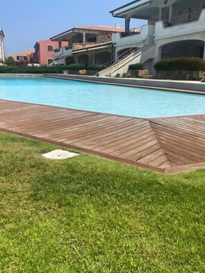 Une piscine dotée d’une terrasse en bois, entourée d’une pelouse bien entretenue et d’un mur de pierres.