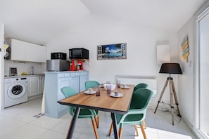 Cocina compacta con lavadora, microondas y comedor con mesa de madera y sillas verdes.