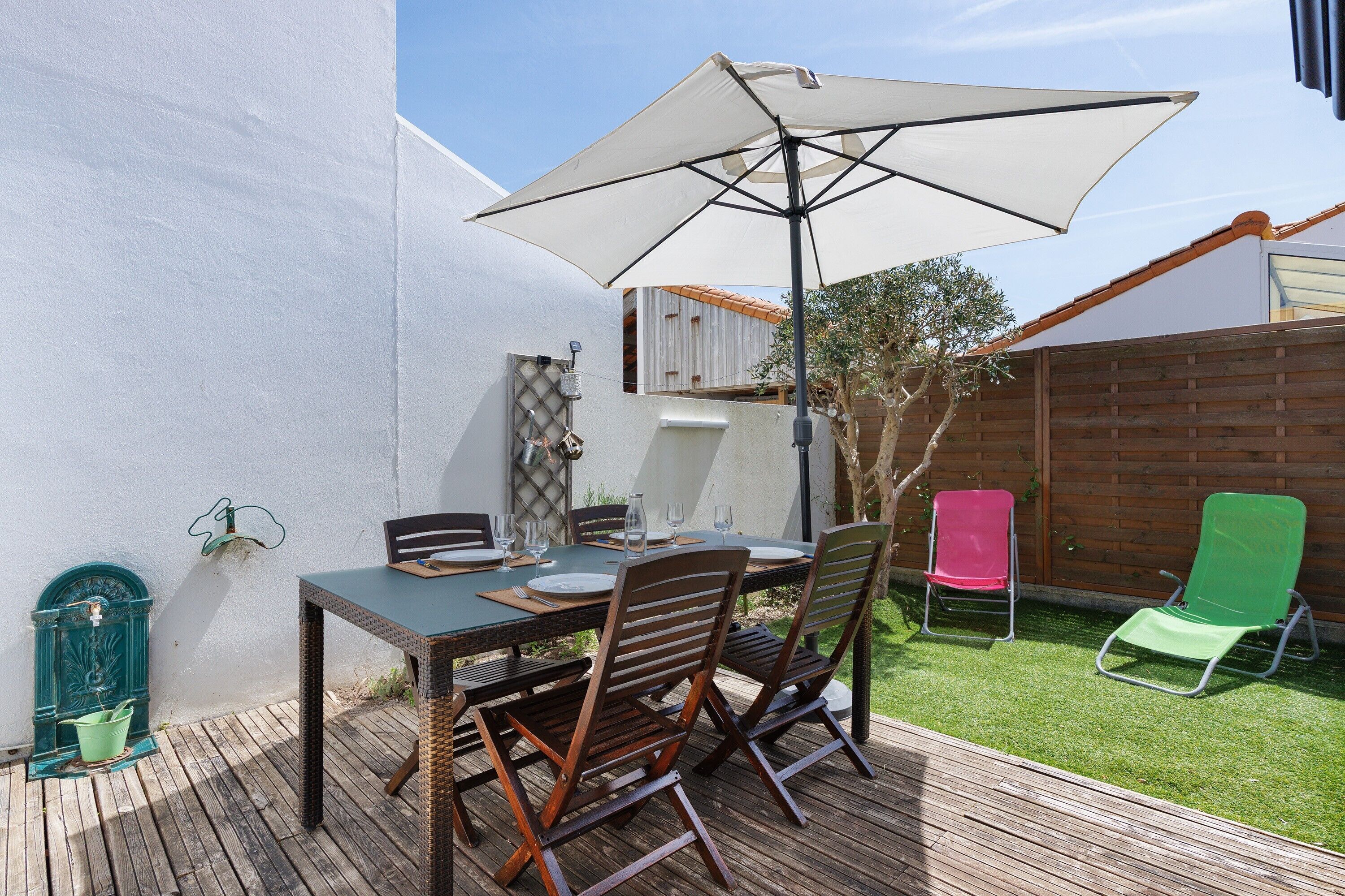 Een terras buiten met een tafel, stoelen, een grote parasol en een houten omheining.