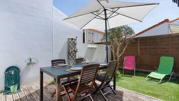 Een terras buiten met een tafel, stoelen, een grote parasol en een houten omheining.