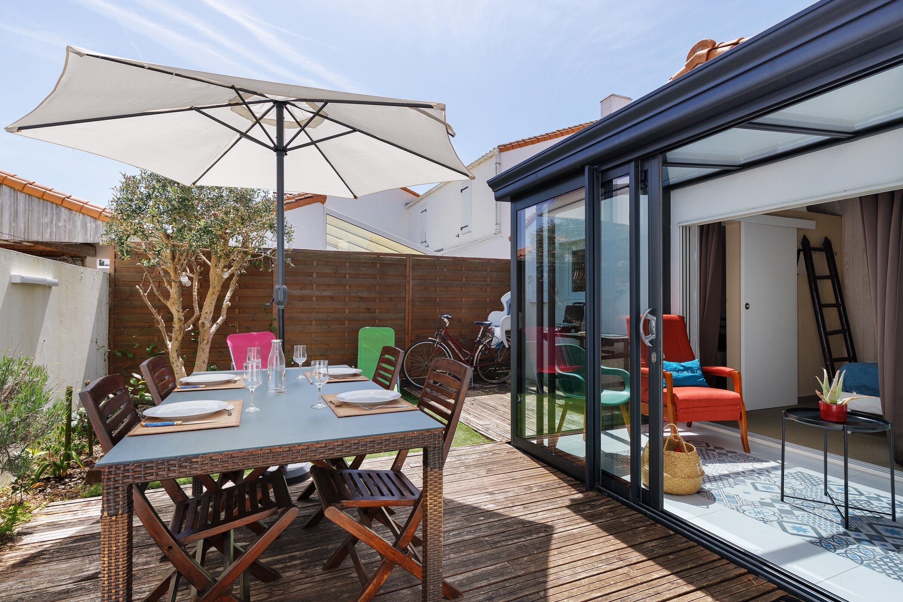 An outdoor patio with a table set for dining, a large umbrella, and a glass-enclosed area with seating.