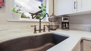 A kitchen with a stainless steel sink, white cabinets, a window with a view, and a coffee maker. - Pet haven near Eugene | Fenced backyard (Creswell)