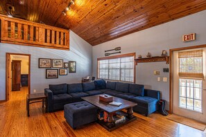 A spacious living room with a sectional sofa, wooden flooring, a ceiling fan, and an exit sign.