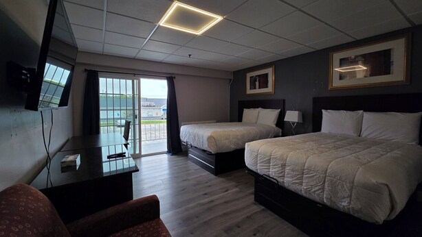 A hotel room with two beds, a desk, a chair, a TV, and a view through a sliding door. - Saffron Inn (Auburn)