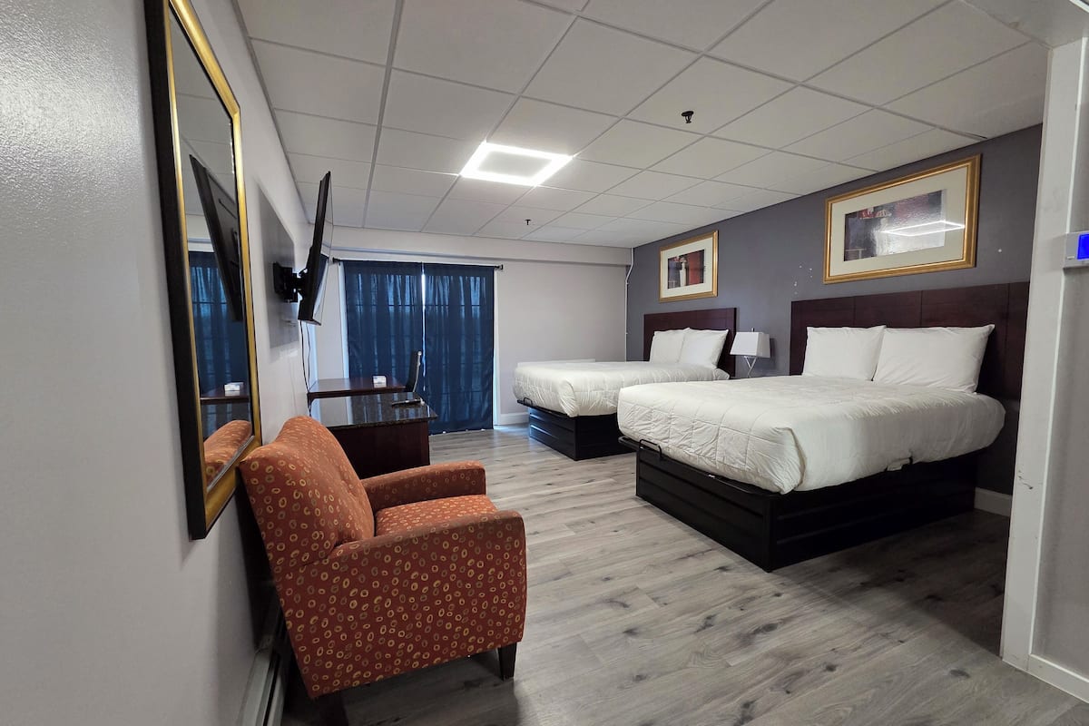 A hotel room with two beds, a desk, a chair, a TV, and a window with curtains.