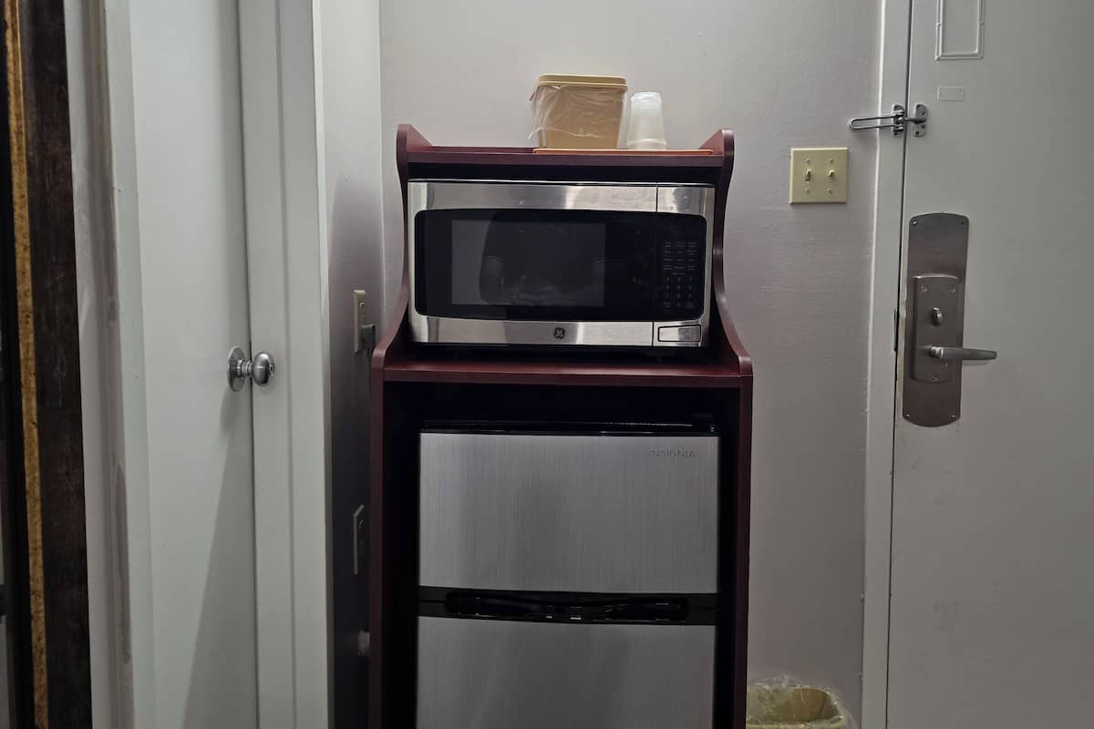 A compact kitchenette with a microwave and refrigerator, a trash bin, and a door with a lock.