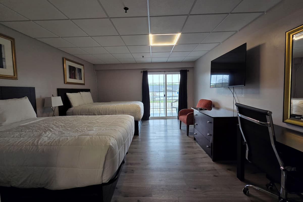 A hotel room with two beds, a desk, a chair, a TV, and a large window.