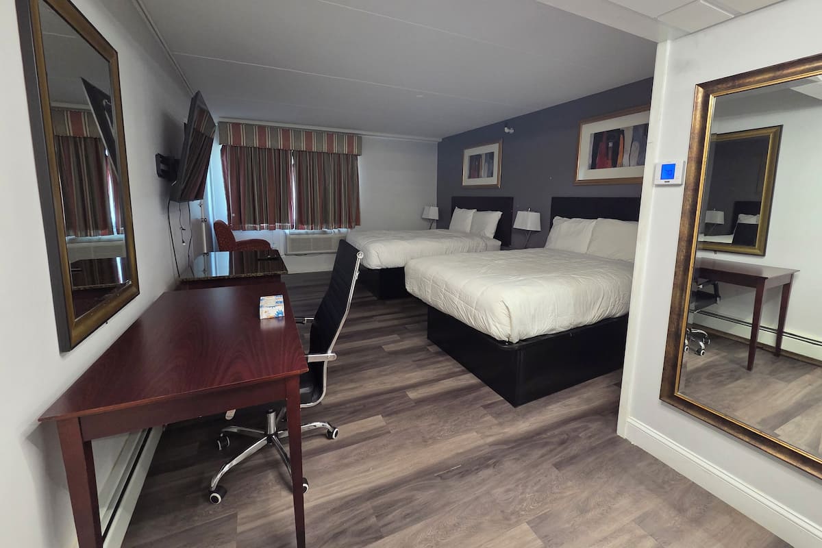 A hotel room with two beds, a desk, a chair, a mirror, and a window with curtains.