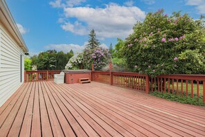 Eine Holzterrasse mit roter Geländer, einem Whirlpool und Blick auf Bäume und Himmel.