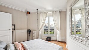 Ein Schlafzimmer mit einem Bett, einem Schminktisch, einem Heizkörper und einem Fenster mit Vorhängen.