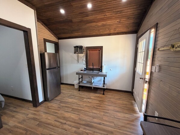 A compact kitchen with a built-in microwave, a stainless steel refrigerator, and a wooden ceiling.