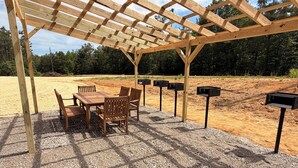 Una estructura de pérgola de madera con una mesa y sillas debajo, rodeada de un área de grava con buzones.