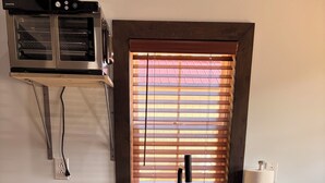 Una cocina con horno empotrado, ventana con persianas, un lavamanos y encimera con varios objetos.
