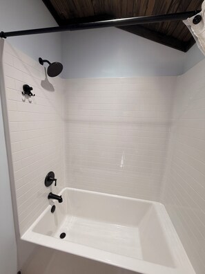 A white-tiled shower with a handheld showerhead, a wall-mounted faucet, and a bathtub.