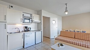 A compact kitchen with a microwave, coffee maker, and a small refrigerator. There is a dining area with a sofa and a table, and a round mirror on the wall. - Beach Flat With Pool (Plougonvelin)