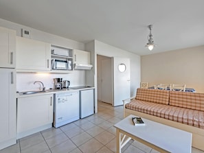 Una cocina compacta equipada con microondas, cafetera y un refrigerador pequeño. Hay un área de comedor con un sofá y una mesa.