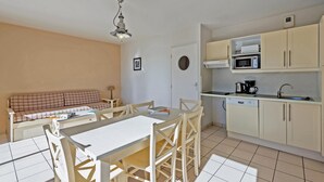 A compact kitchen with a dining area, a sofa, and a single light fixture. - Beach Flat With Pool (Plougonvelin)