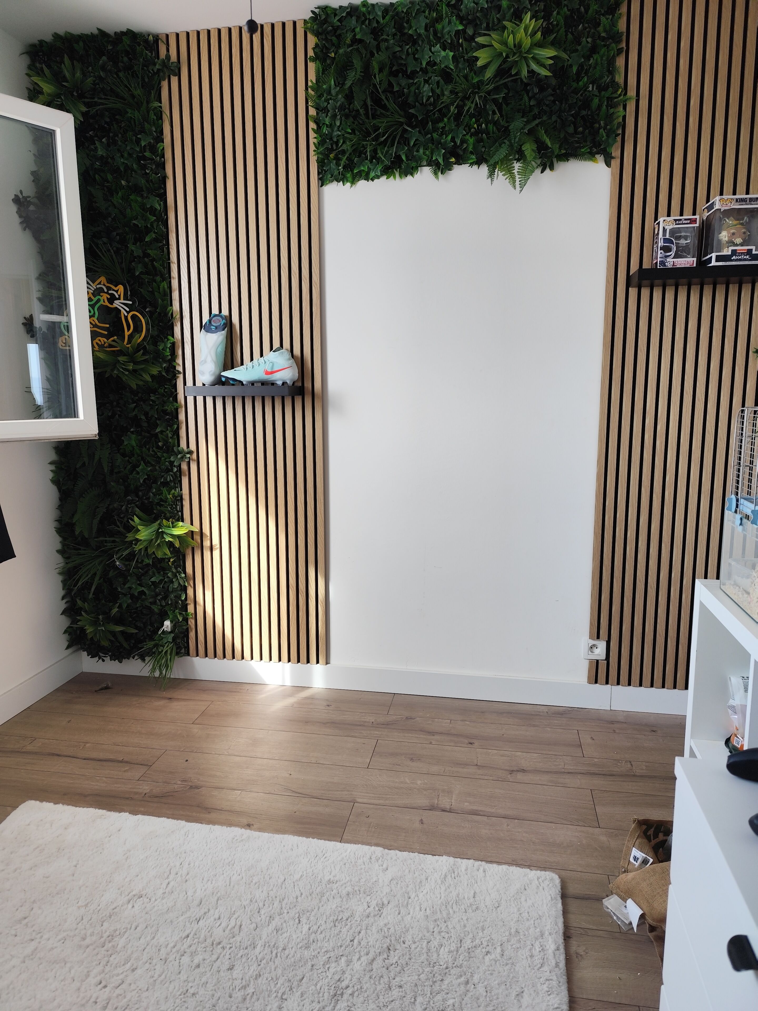 A room with a wooden floor, white walls, a white rug, a vertical wooden slat wall, and a green plant wall.
