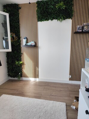 A room with a wooden floor, white walls, a white rug, a vertical wooden slat wall, and a green plant wall. - Quiet house in a family subdivision, close to village, sea and walks... (Roquebrune-sur-Argens)