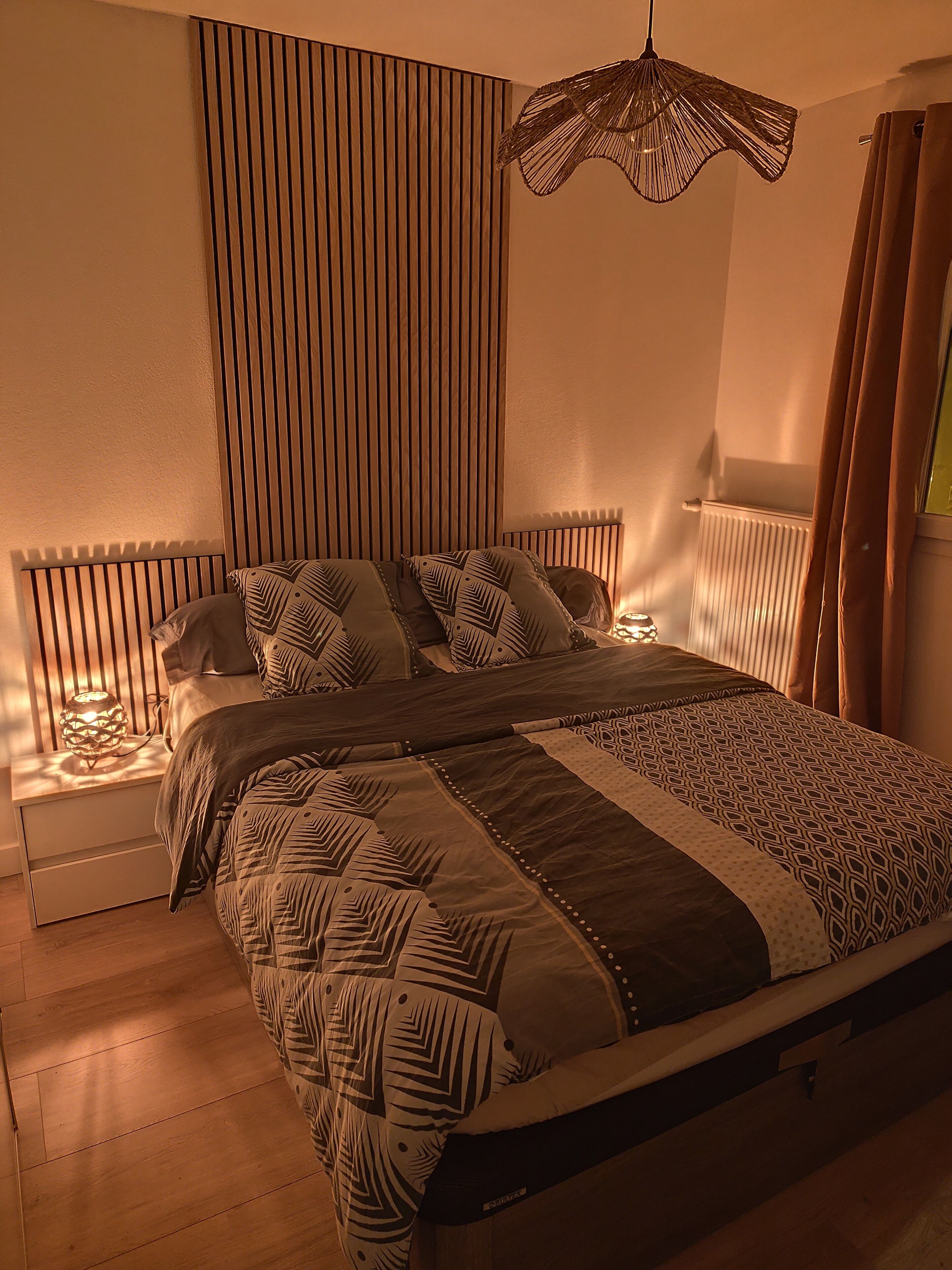 A modern bedroom with a bed, bedside tables, a hanging light fixture, and a radiator.