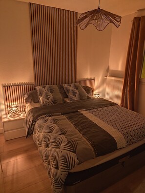 Ein modernes Schlafzimmer mit einem Bett, Nachttischen, einer Pendelleuchte und einer Heizung.
