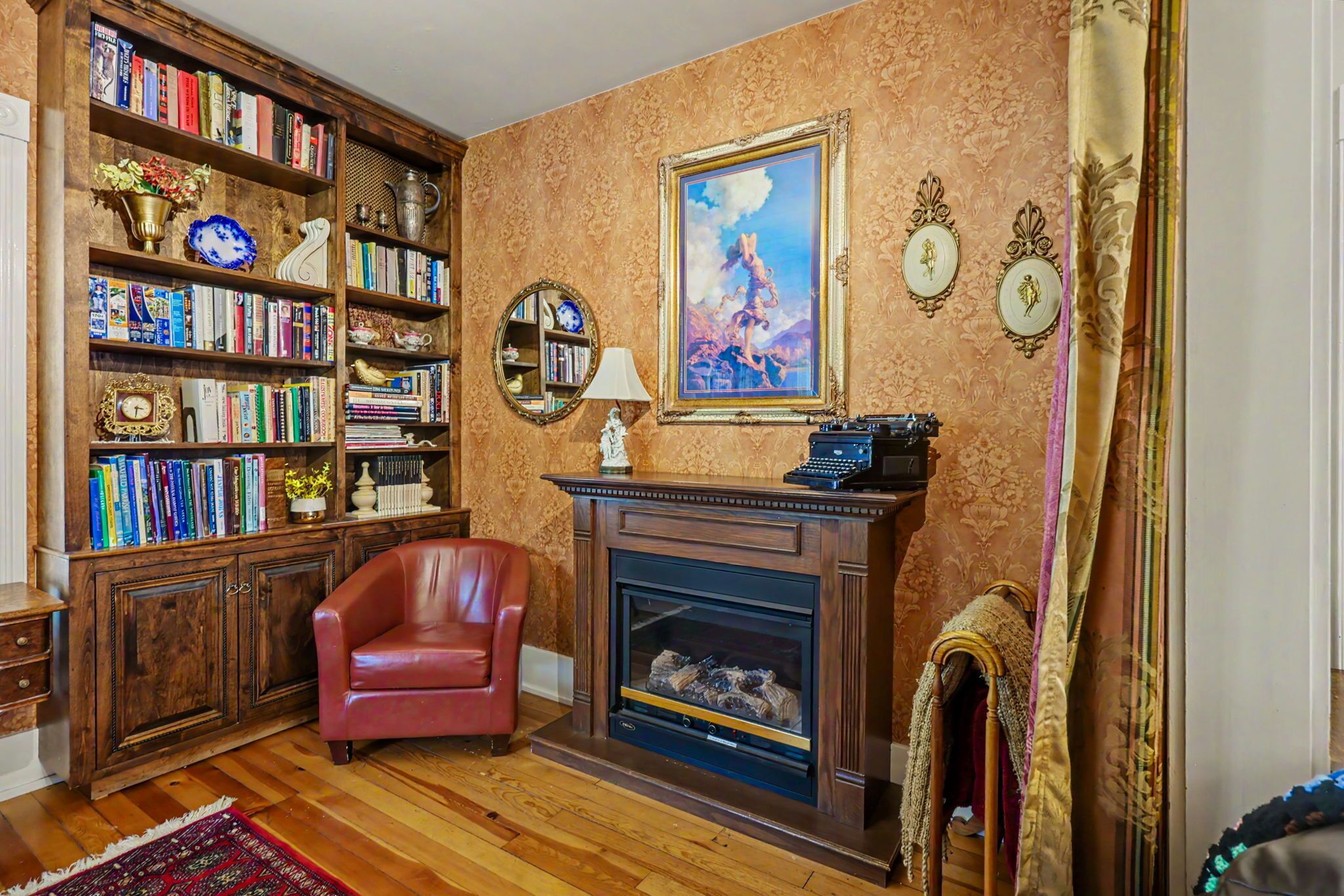 Ein Zimmer mit Kamin, Bücherregalen, einem roten Sessel und einem großen gerahmten Gemälde.