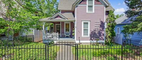 A two-story house with a porch, a fenced yard, and a clear sky.