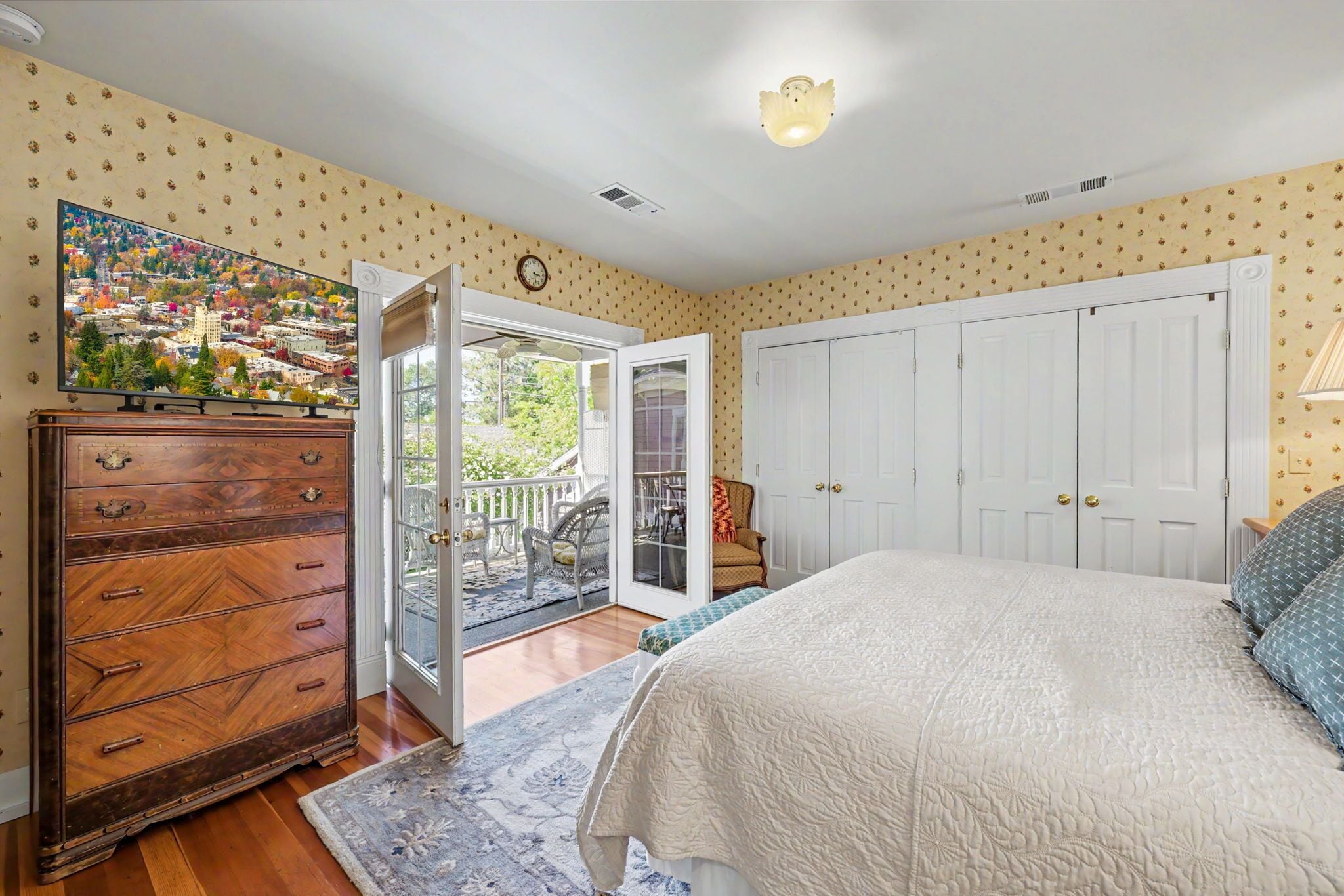 A bedroom with a large bed, a dresser, a painting, and a door leading to a balcony.