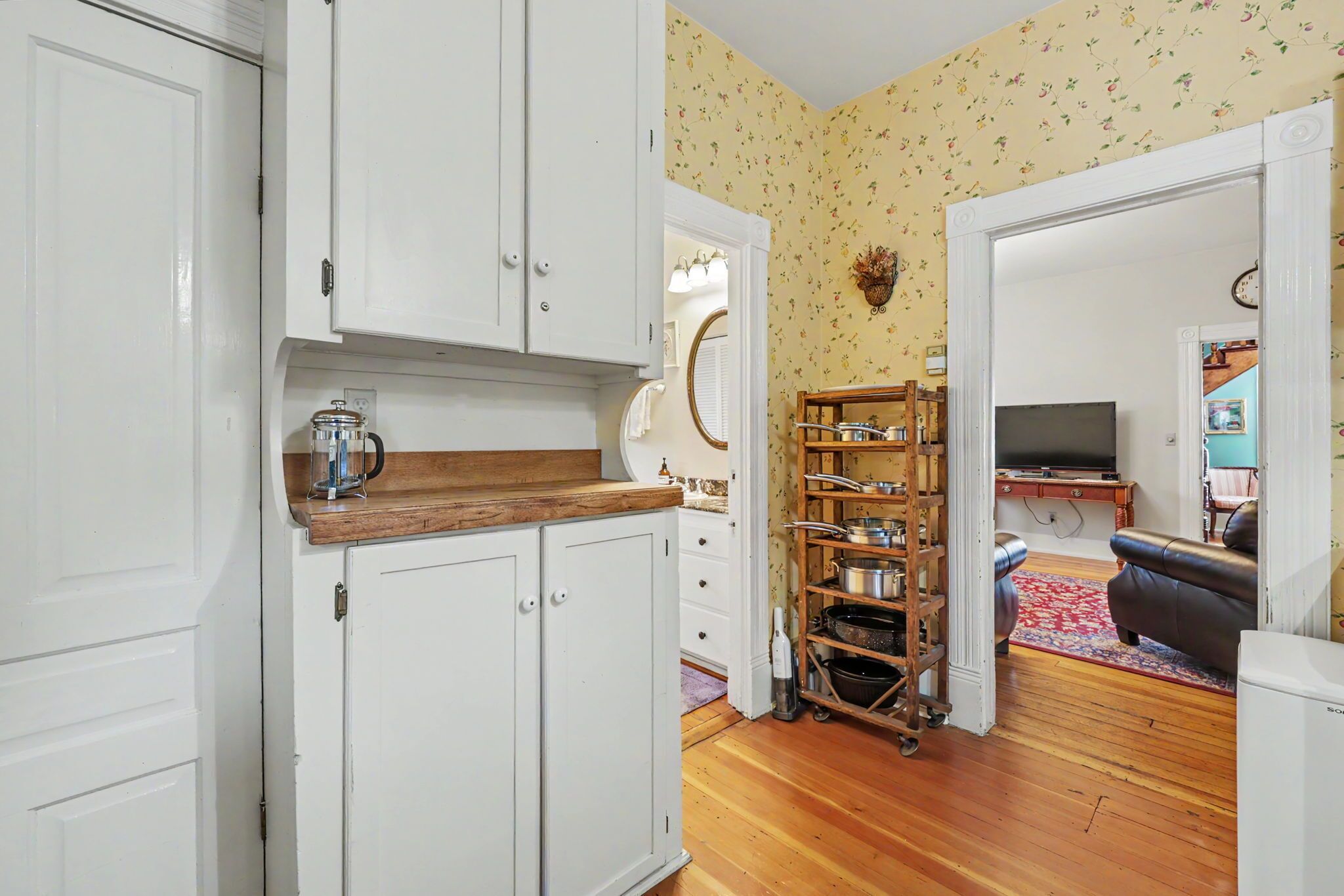 A kitchen with white cabinets, a wooden countertop, and a pot rack.