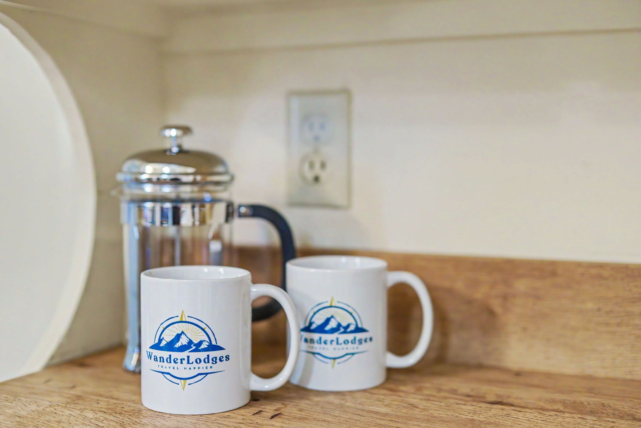 Two white mugs with 'WanderLodges' logo on a wooden shelf.