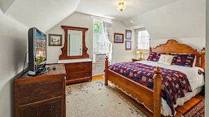 Un dormitorio con cama, cómoda, televisor y ventana con cortinas.