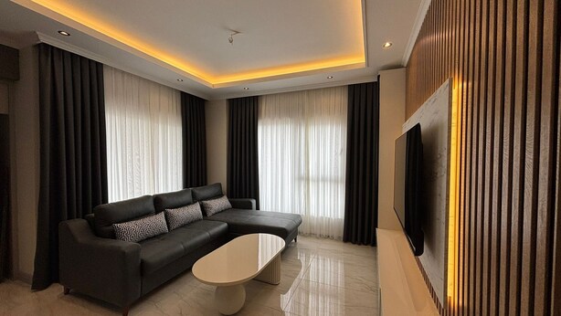 A modern living room with a sectional sofa, a coffee table, a flat-screen TV, and a wooden accent wall. - Luxury apartment in Alanya with 270° panoramic views & only 5 min to the beach (Kargicak)
